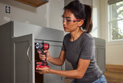 Person using CRAFTSMAN cordless impact driver model CMCF610B to install hardware on gray cabinet, indoor setting.