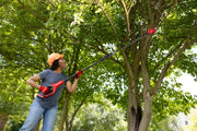 Person using CRAFTSMAN pole saw, model CMCPPR320B, trimming tree branches outdoors.