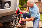 Photo of a person cleaning a car tire with a Craftsman power scrubber, SKU CMCPSMB, outdoors on a driveway.