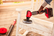 Photo of person cleaning a white wooden chair with Craftsman cordless scrubber, SKU CMCPSMFB, outdoor setting.